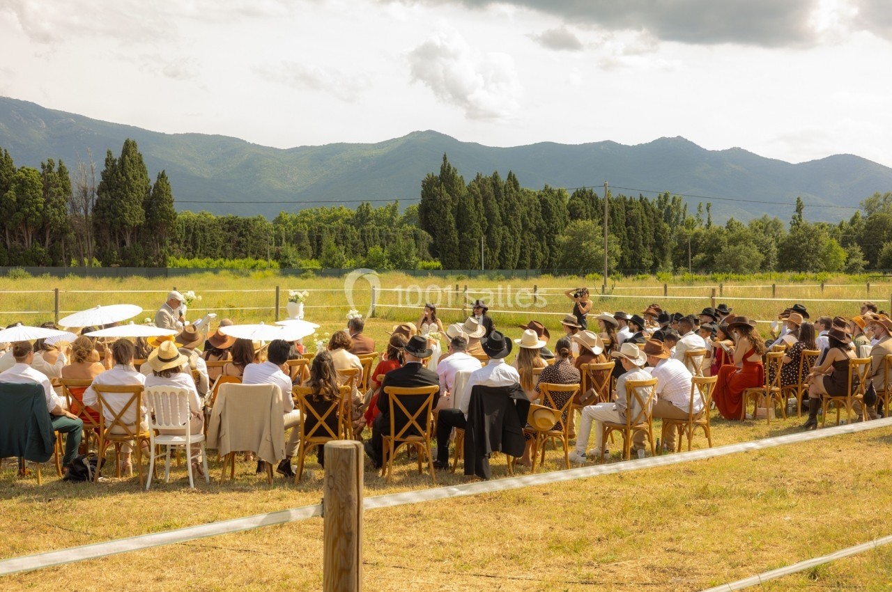 Groupe de personnes assises en extérieur lors d'un événement, avec des montagnes et des arbres en arrière-plan.