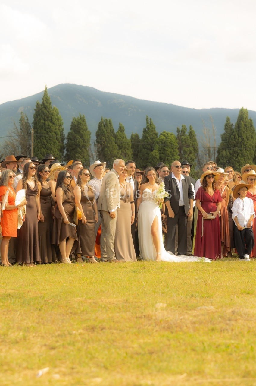 Un groupe de personnes, dont un couple en tenue de mariage, pose en extérieur devant un paysage montagneux.
