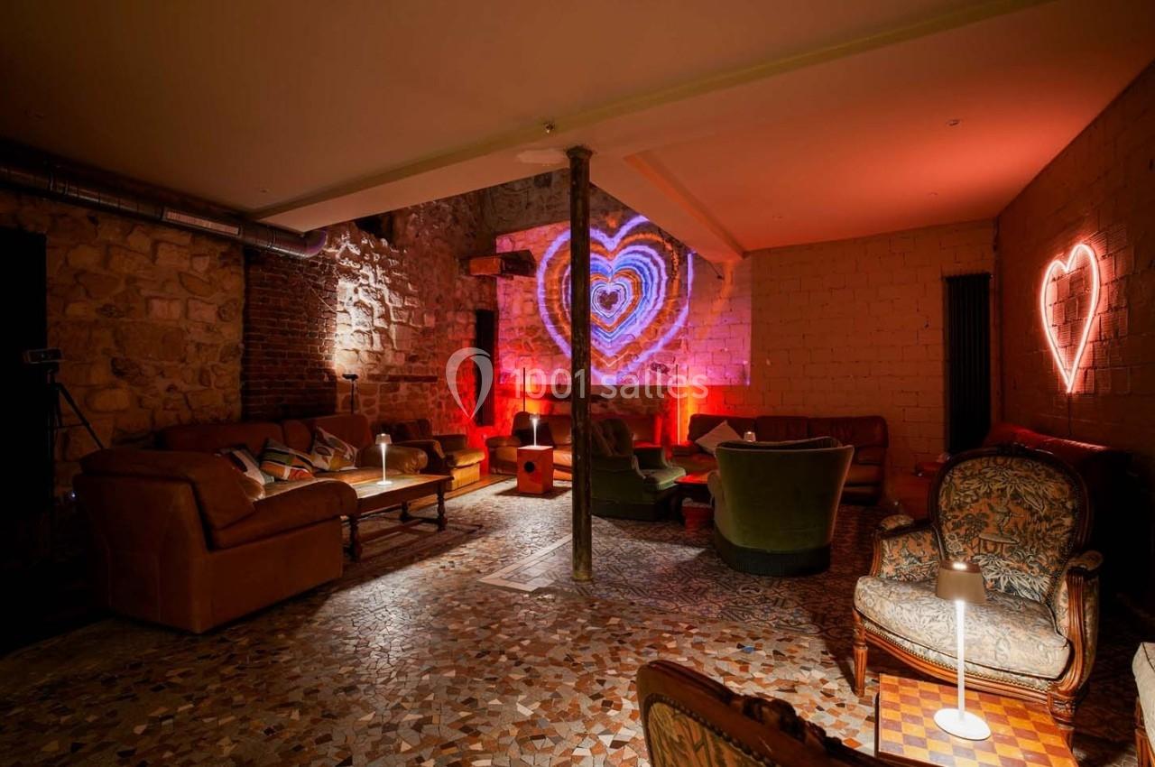 Salle cosy avec murs en pierre, fauteuils et canapés, éclairage tamisé et décorations lumineuses en forme de cœur.