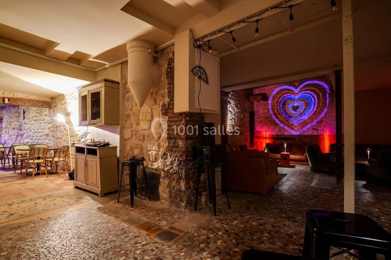 Salle voûtée avec murs en pierre, mobilier éclectique et projection lumineuse en forme de cœur sur un mur.