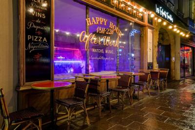 Miniature Location salle Nanterre (Hauts-de-Seine) - Les Enfants Terribles #14 Façade d'un café-restaurant avec terrasse vide, éclairée par des lumières colorées en soirée pluvieuse.