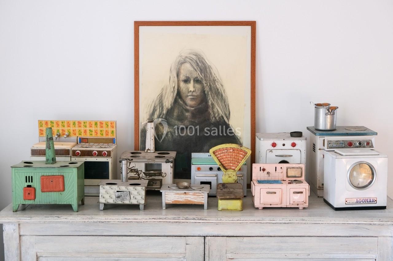 Collection de jouets anciens représentant des cuisinières miniatures, disposée sur un meuble devant un portrait encadré.
