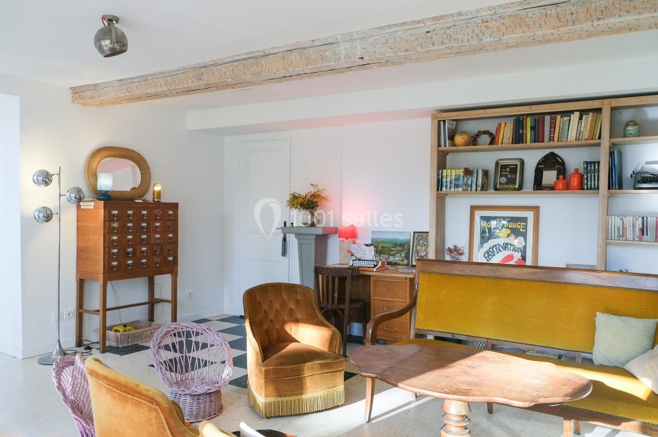 Salon lumineux avec poutres apparentes, mobilier vintage, étagères remplies de livres et objets décoratifs.