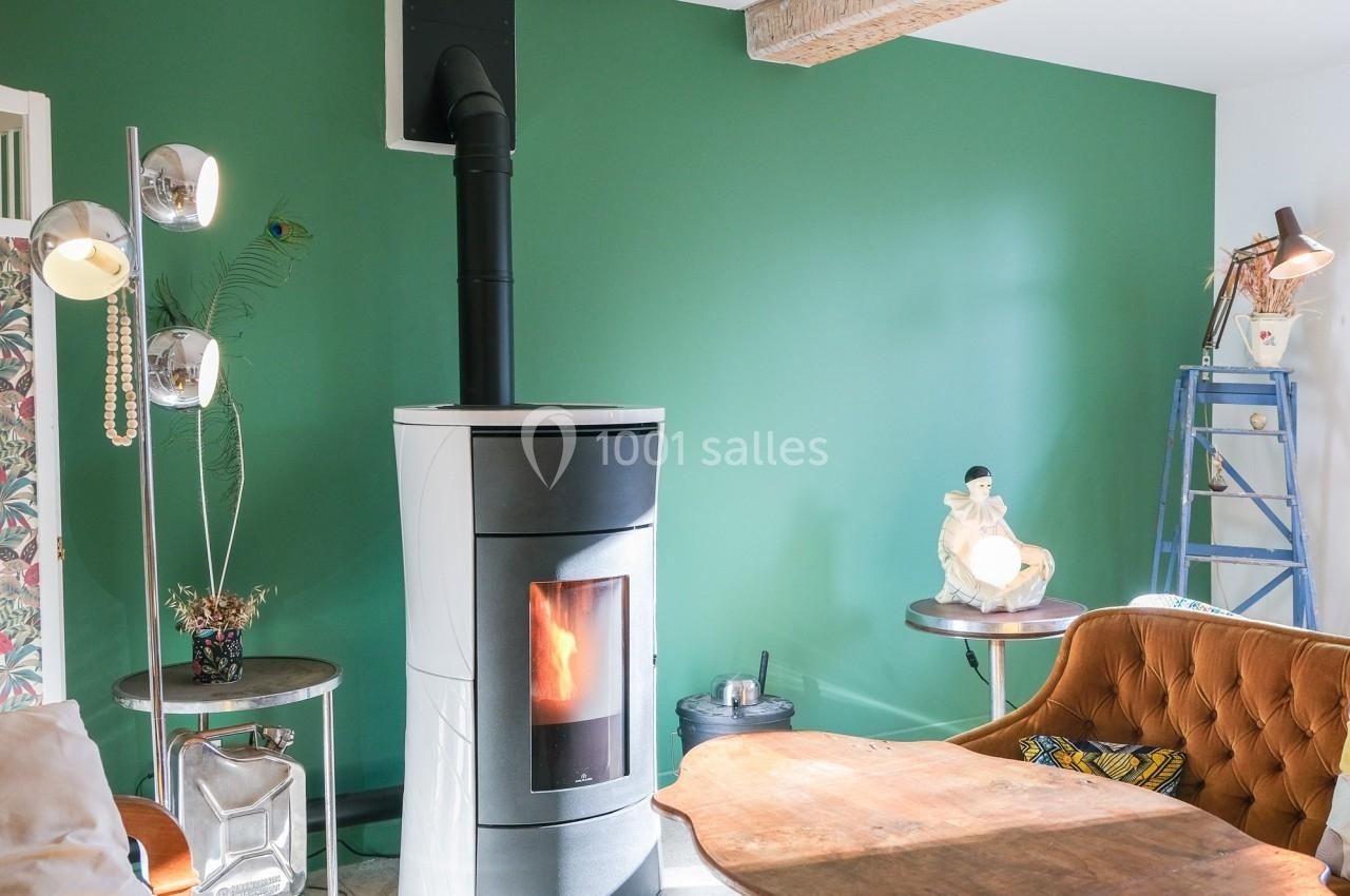 Poêle à bois moderne allumé dans un salon avec mur vert, mobilier vintage et décoration éclectique.