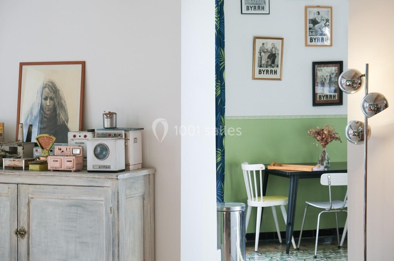 Intérieur éclectique avec un buffet ancien, des objets rétro, et un coin repas aux murs verts décorés de cadres.
