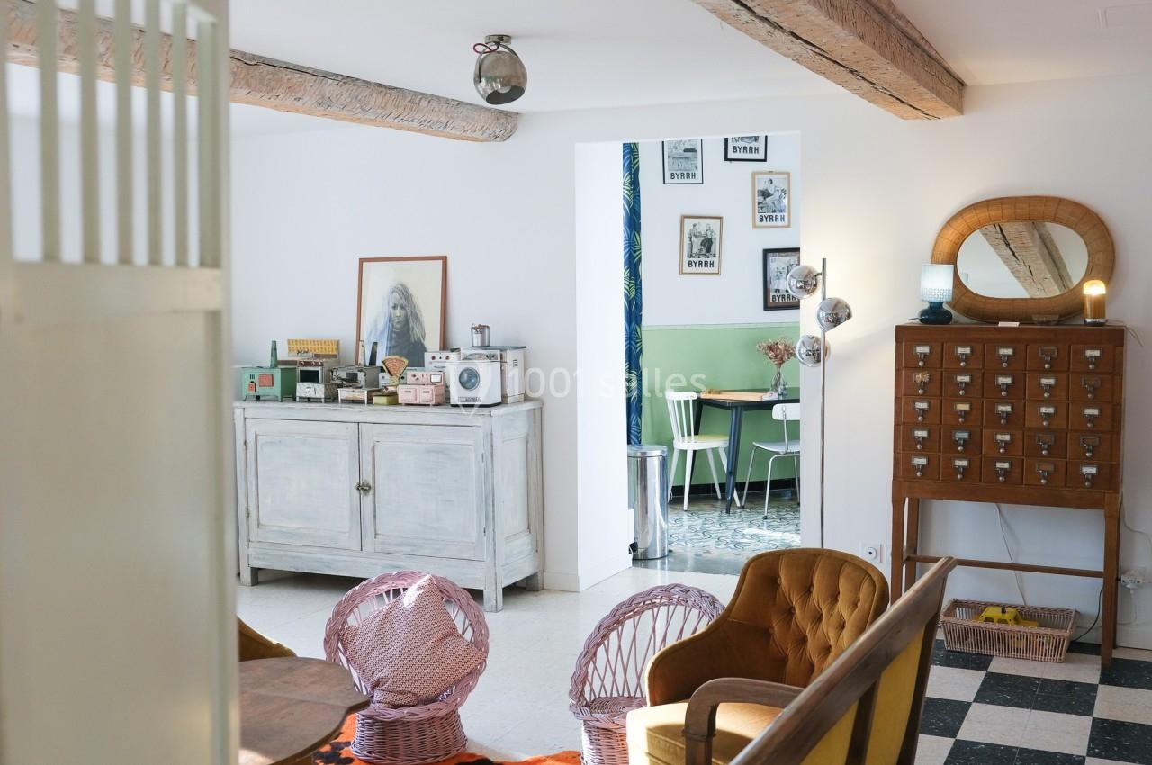 Intérieur lumineux avec mobilier vintage, fauteuils colorés, buffet blanc et vue sur une salle à manger rétro.