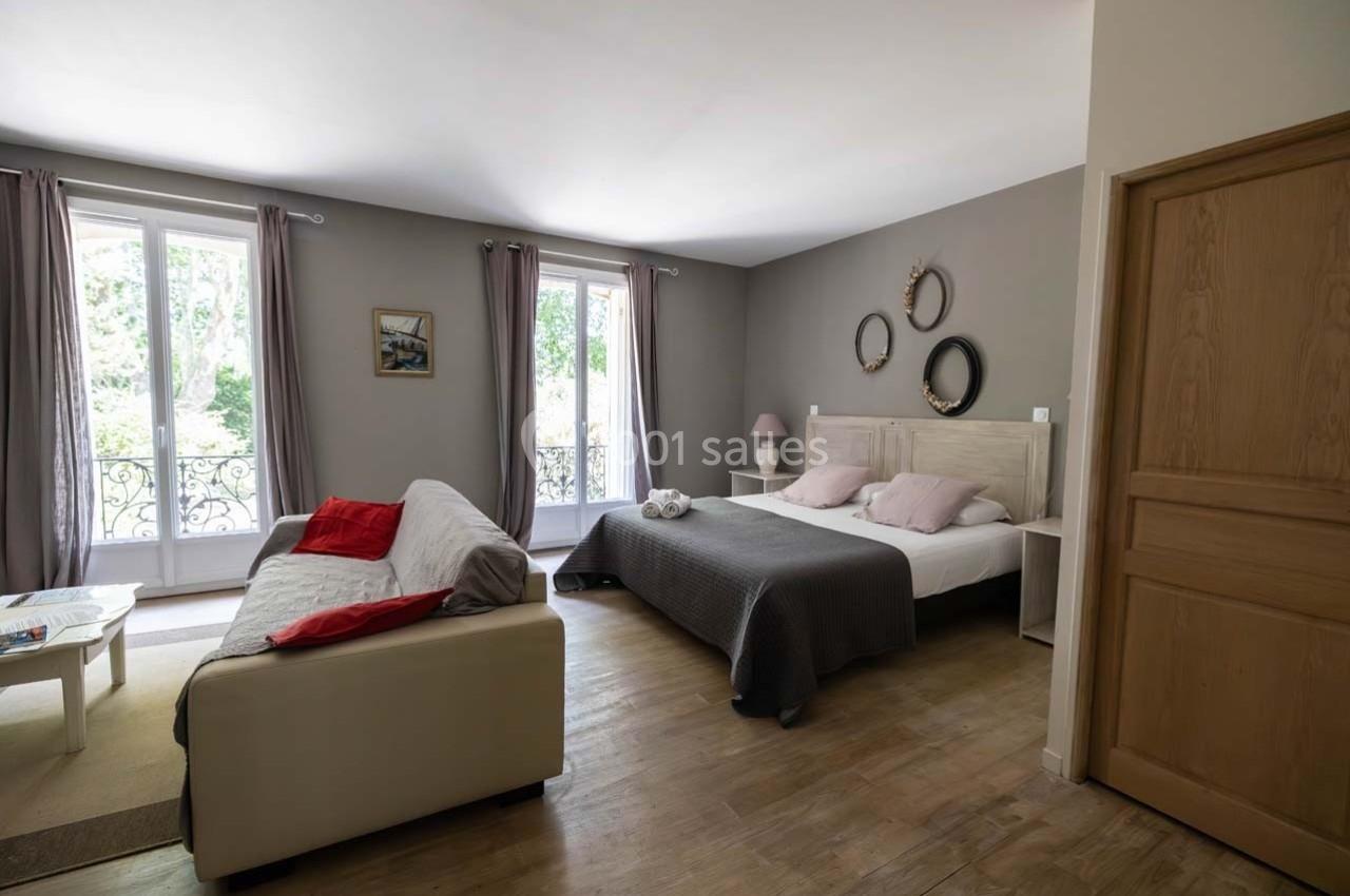 Chambre lumineuse avec lit double, canapé, grandes fenêtres donnant sur un jardin et décoration sobre.