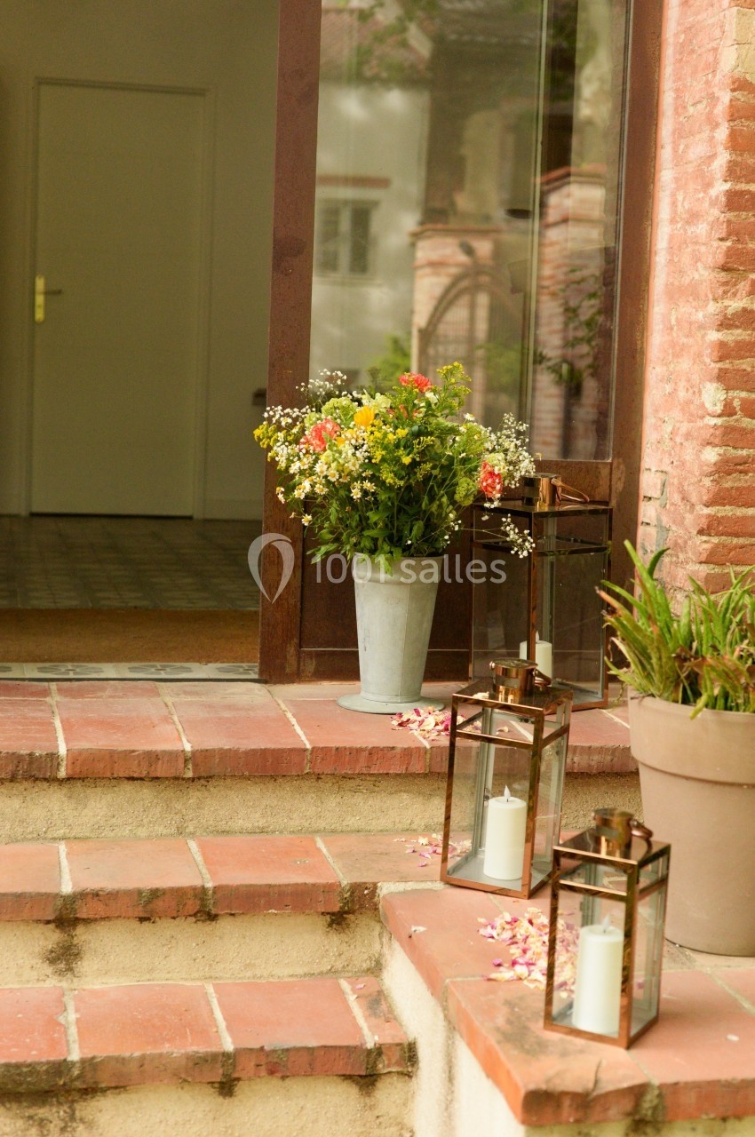 Pot de fleurs colorées et lanternes avec bougies sur des marches en briques devant une porte en verre.
