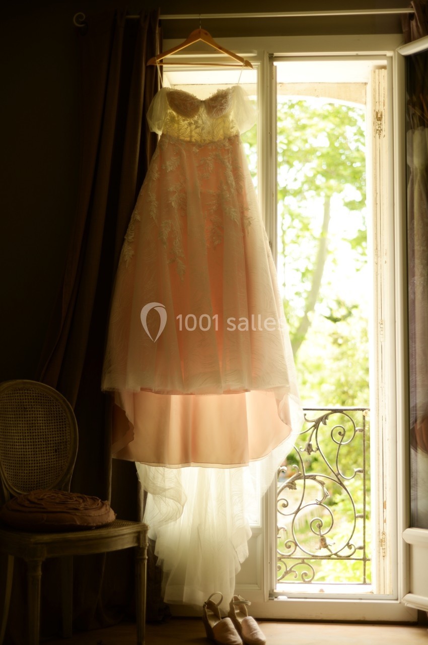 Robe de mariée suspendue à un cintre devant une fenêtre ouverte, laissant entrer la lumière naturelle.