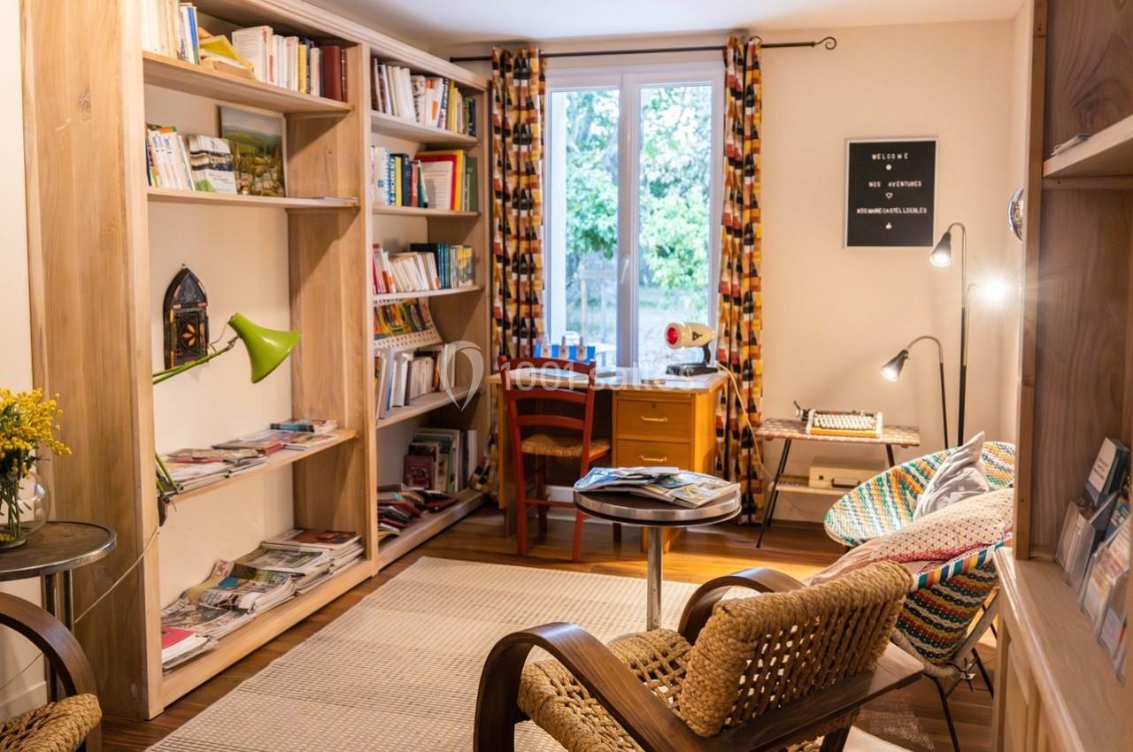 Salon lumineux avec bibliothèque en bois, bureau près d'une fenêtre, fauteuils en osier et décoration colorée.