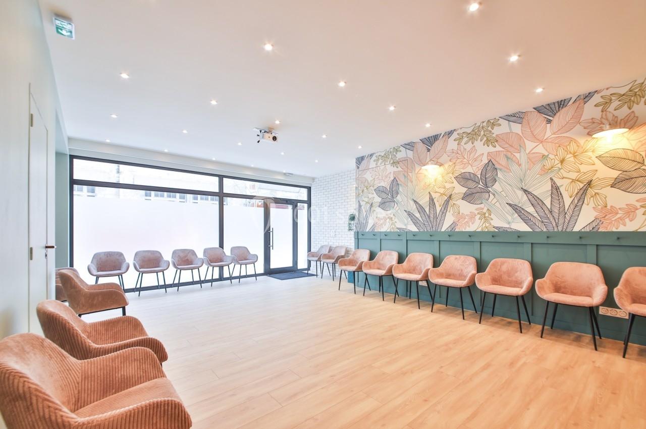 Salle d'attente lumineuse avec chaises roses alignées, mur décoré de motifs floraux et grande baie vitrée.