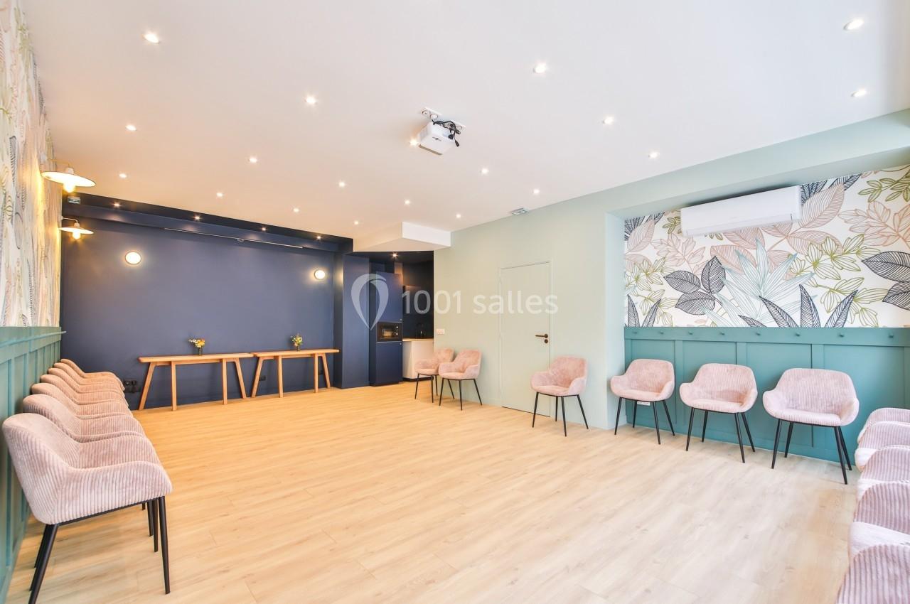 Salle lumineuse avec parquet clair, murs décorés de motifs floraux et rangées de chaises roses alignées.