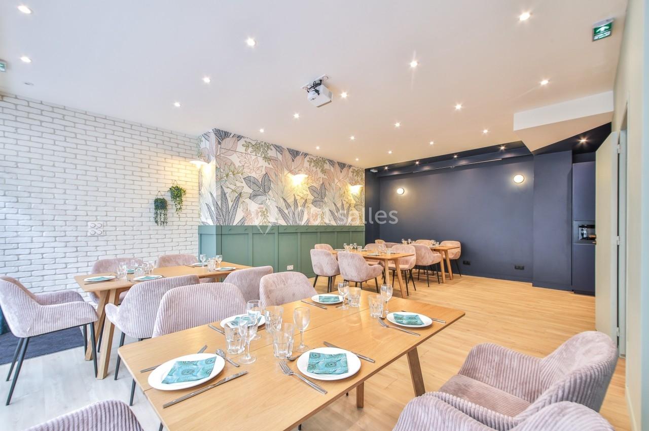 Salle de restaurant lumineuse avec tables en bois, chaises rembourrées et mur décoré de motifs végétaux.