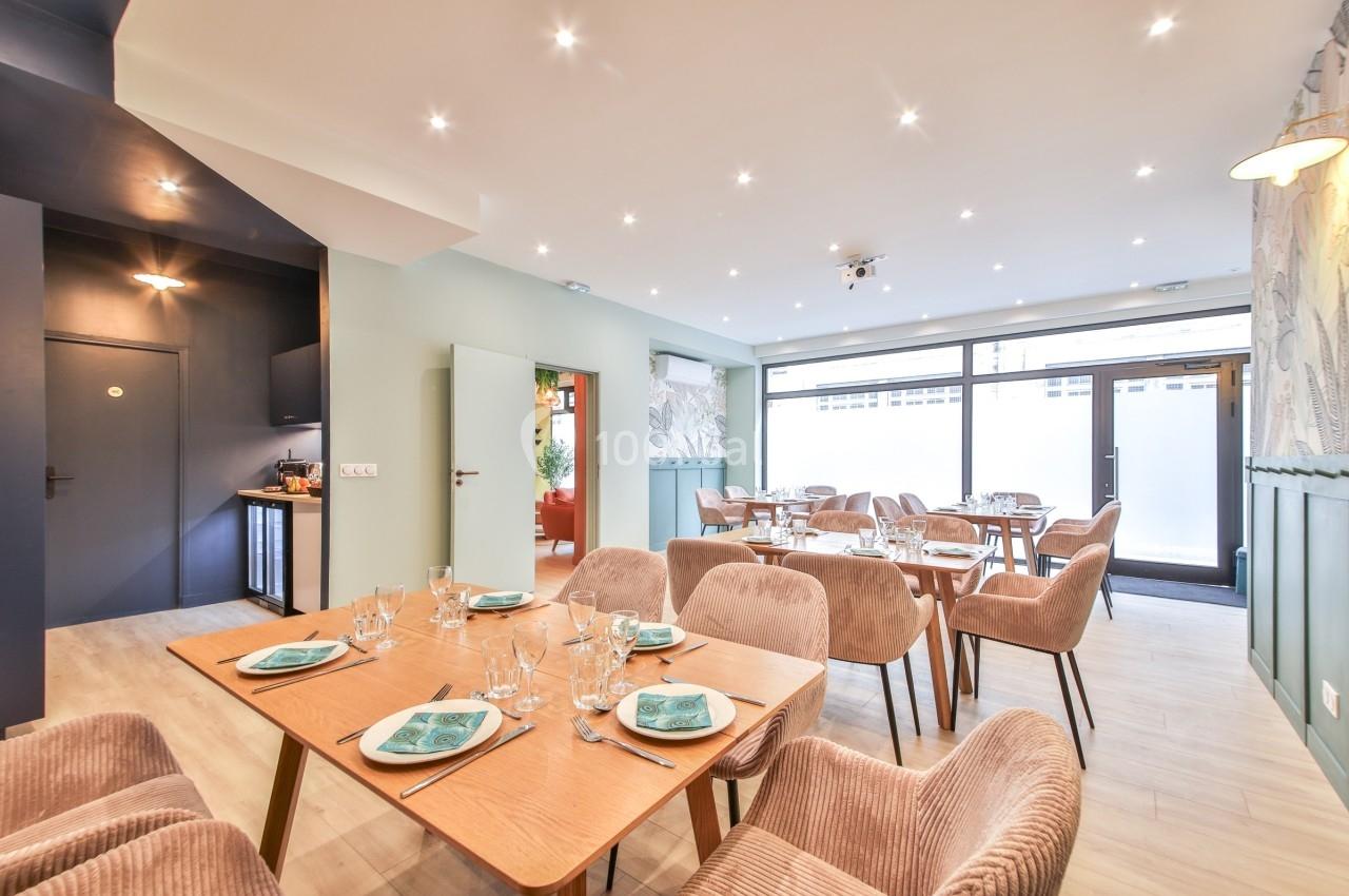 Salle de restaurant lumineuse avec tables en bois, chaises rembourrées et vaisselle dressée, vue sur une grande baie vitrée.