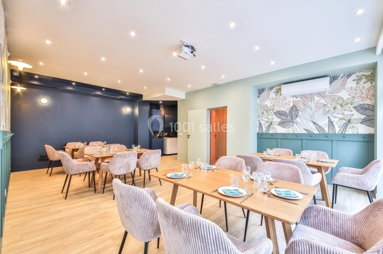Salle lumineuse avec tables en bois, chaises rembourrées, murs bleu foncé et décor floral sur un pan de mur.