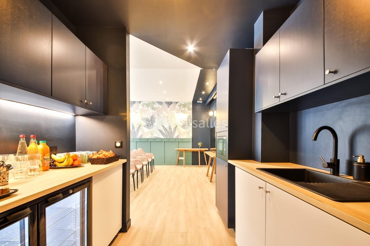 Cuisine moderne avec meubles bleu foncé, plan de travail en bois clair, évier noir et boissons disposées sur un comptoir.