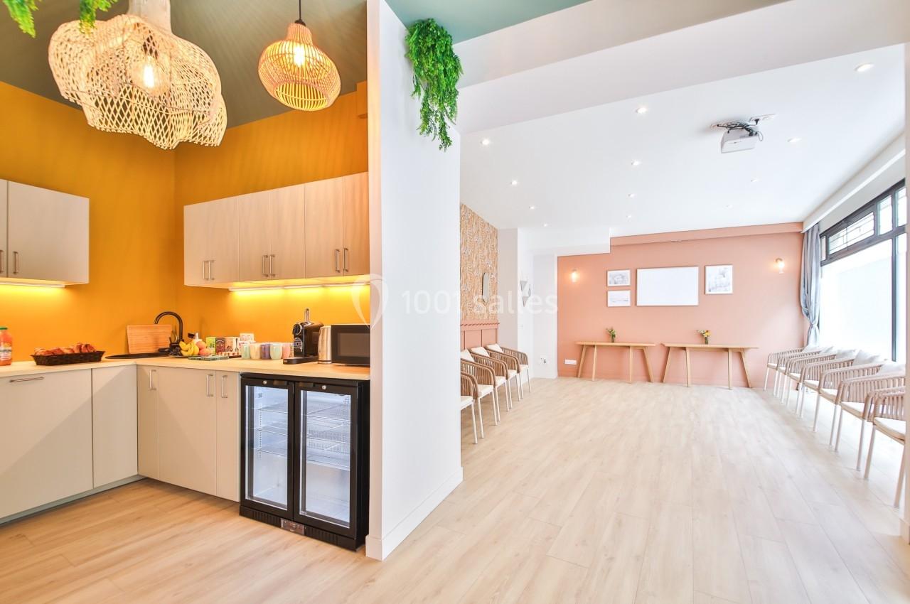 Cuisine moderne ouverte avec éclairage chaleureux, réfrigérateur vitré et espace lumineux avec chaises en arrière-plan.