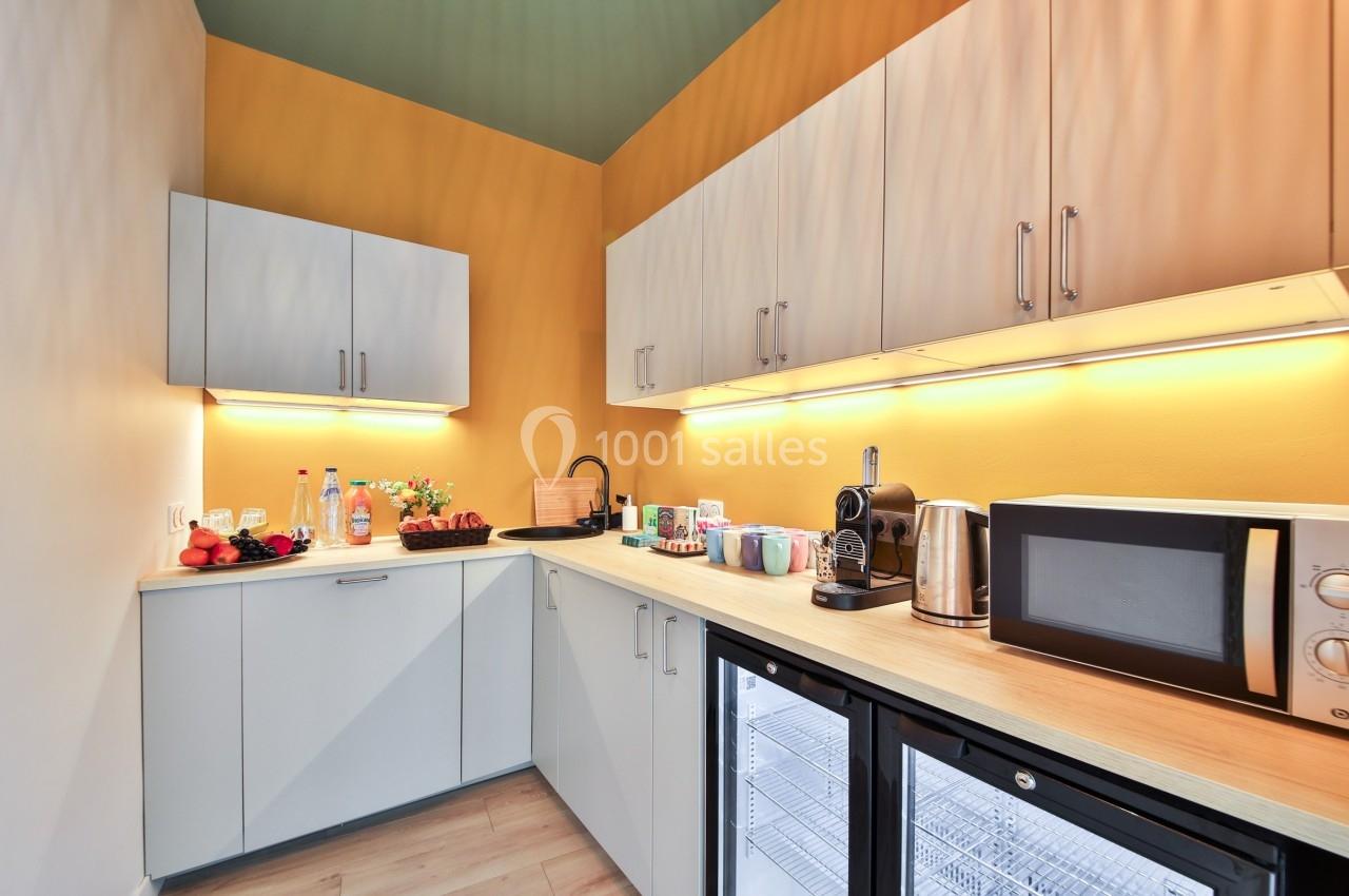 Cuisine équipée avec micro-ondes, cafetière, évier, réfrigérateur, étagères et divers aliments sur le plan de travail.