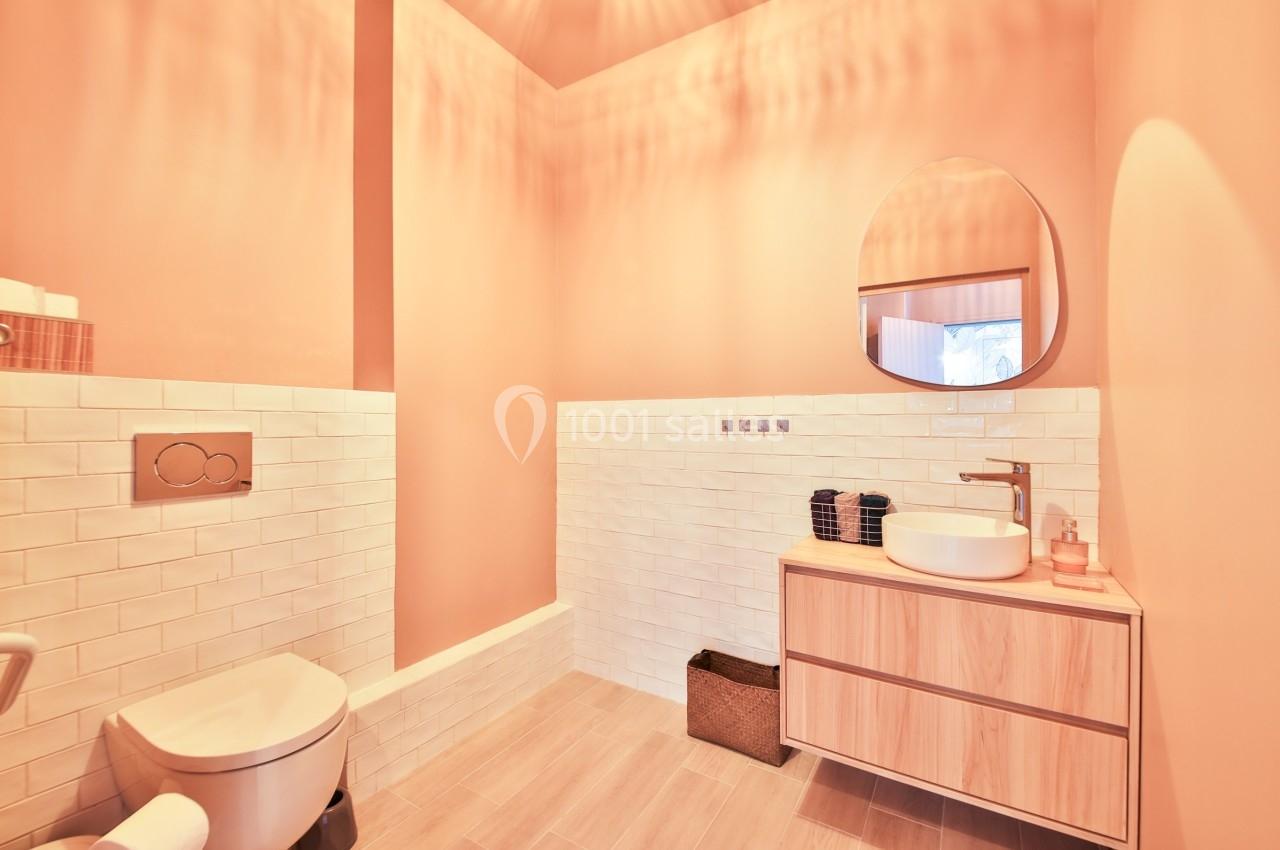 Salle de bain moderne avec murs pêche, lavabo sur meuble en bois, miroir rond et toilettes.