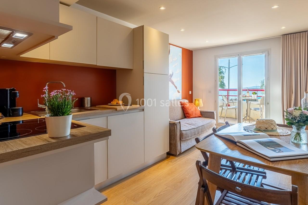 Cuisine ouverte avec table en bois, canapé, balcon ensoleillé et décoration chaleureuse dans un appartement lumineux.