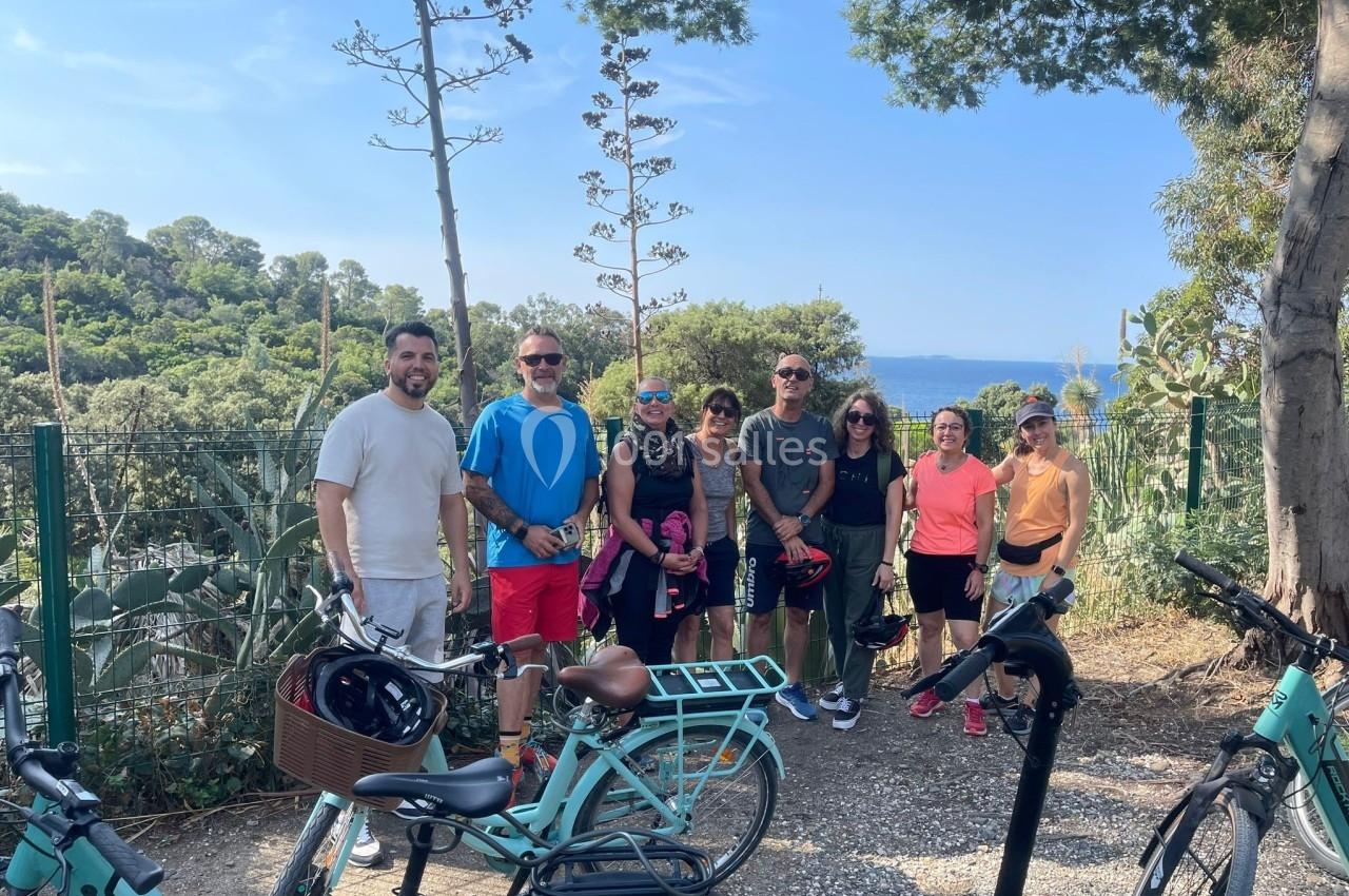 Un groupe de personnes posant avec des vélos devant un paysage boisé et une vue sur la mer.