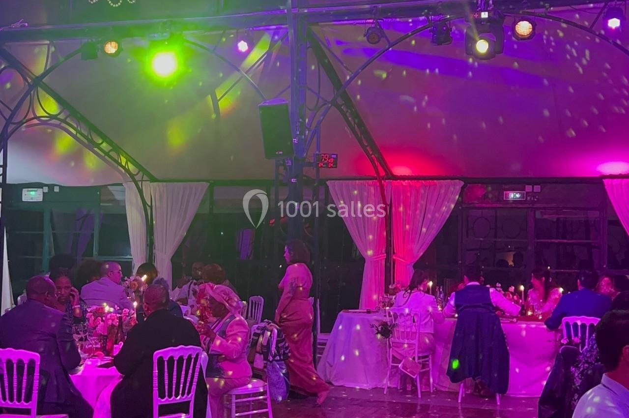 Salle de réception illuminée avec des invités assis à des tables décorées, sous une boule à facettes et des lustres.