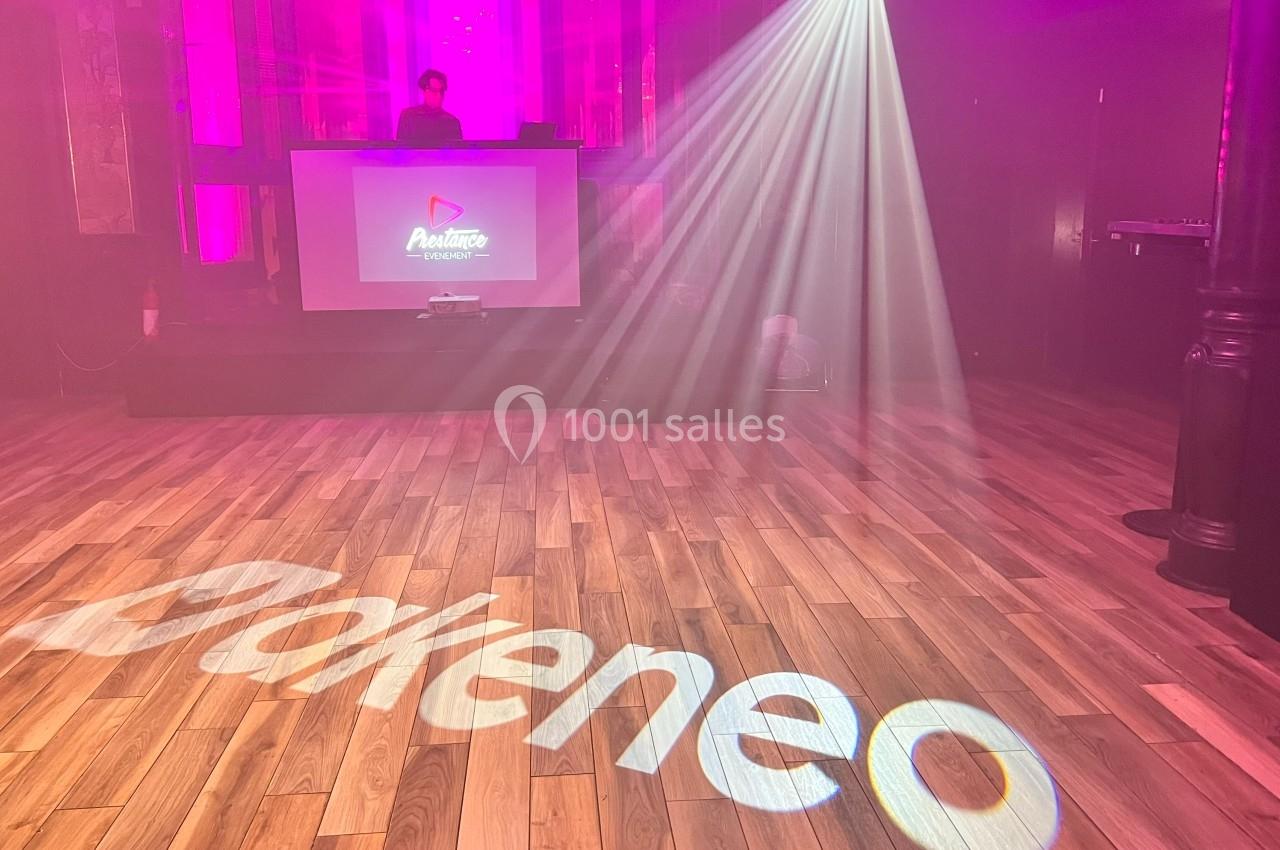 Salle de spectacle avec un DJ sur scène, éclairages colorés et logo ’Akeneo’ projeté sur le sol en bois.