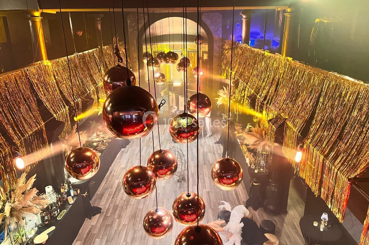 Suspension de boules rouges brillantes dans une salle décorée de guirlandes dorées et éclairée par des lumières chaudes.
