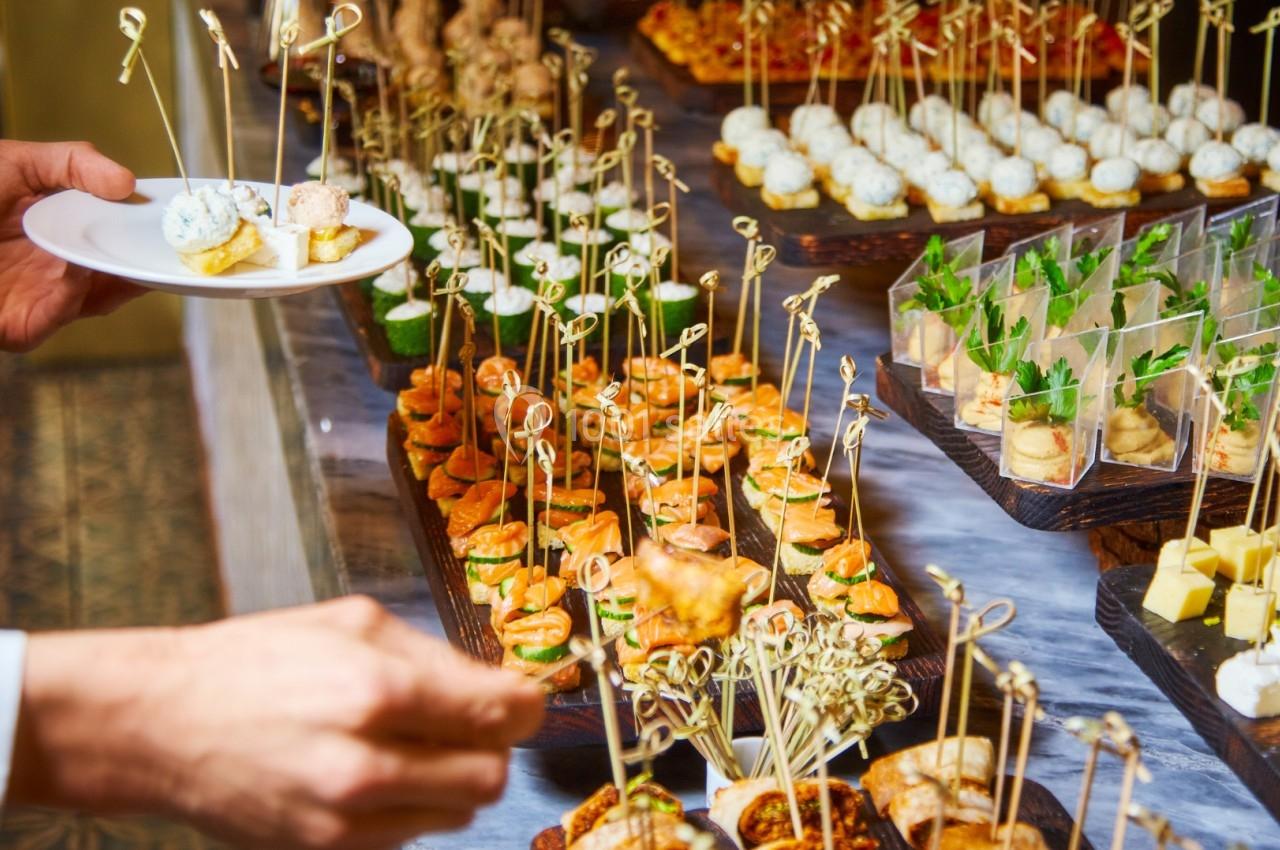 Plateau de bouchées apéritives variées présentées sur des brochettes, avec une personne servant un plat.