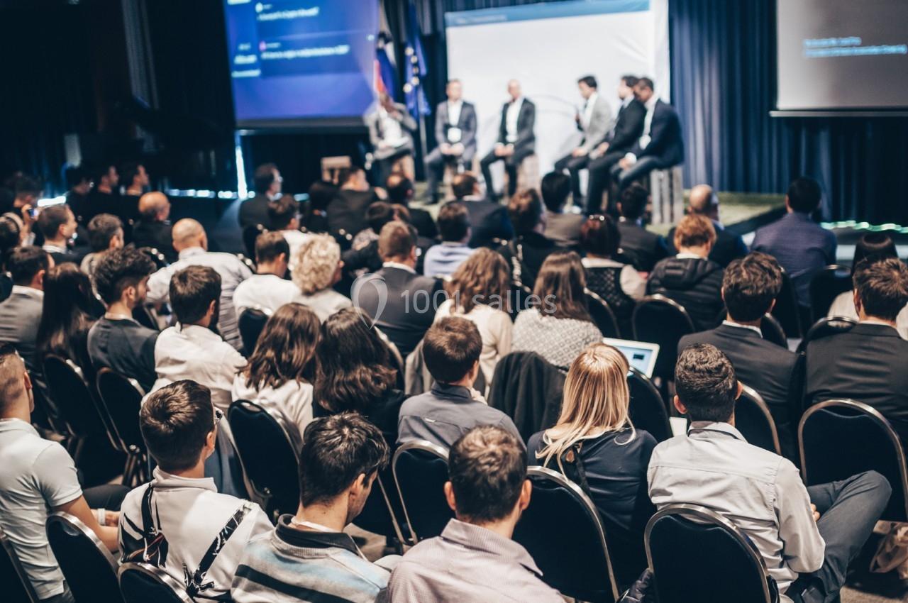 Un public assis écoute un panel de conférenciers sur une scène dans une salle de conférence.