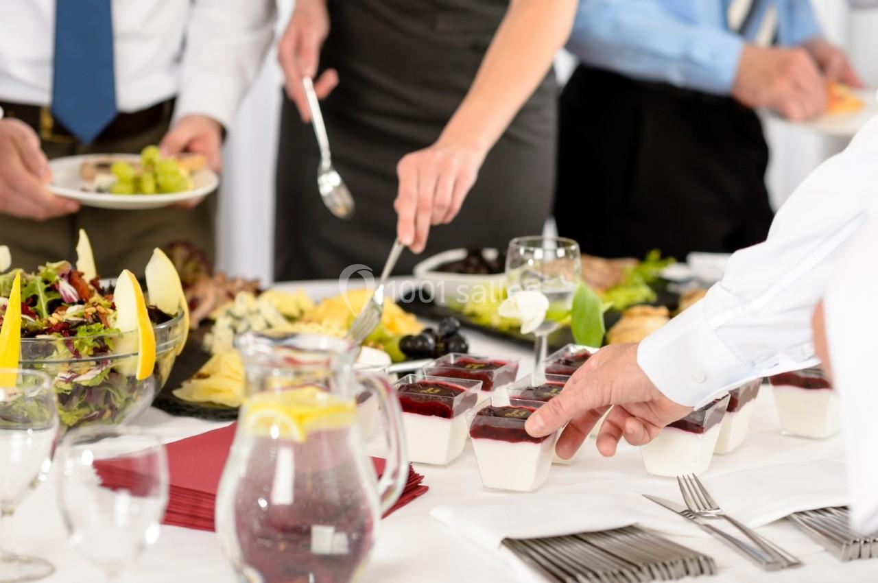 Personnes se servant à un buffet avec des salades, desserts en verrines et carafe d'eau sur une table dressée.