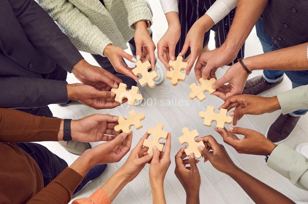 Des mains de personnes diverses tenant des pièces de puzzle en bois, symbolisant la collaboration et l'unité.