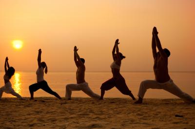 Personnes pratiquant le yoga sur une plage au coucher du soleil, en position debout avec les bras levés.