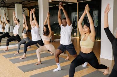 Personnes pratiquant le yoga sur une plage au coucher du soleil, en position debout avec les bras levés.