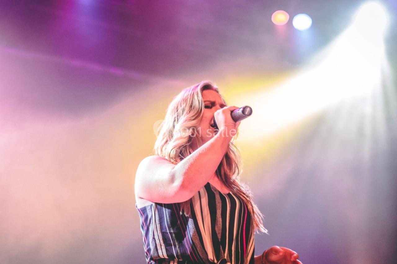 Une femme chante sur scène sous des projecteurs colorés, tenant un micro dans un environnement de concert.