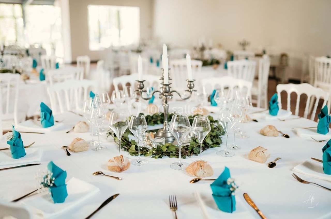 Table de réception élégamment dressée avec nappes blanches, serviettes bleues pliées, bougeoirs et décorations végétales.
