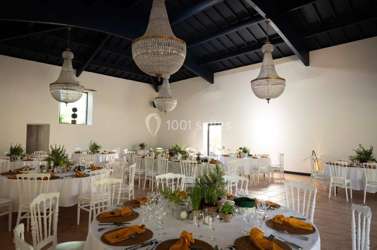 Salle de réception décorée avec des tables rondes, nappes blanches, chaises blanches et lustres en cristal suspendus.