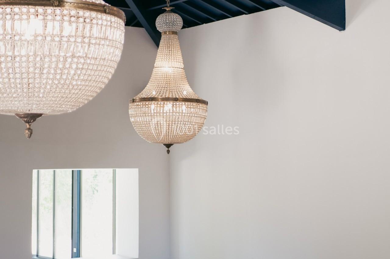 Deux lustres en cristal suspendus dans une pièce lumineuse avec un mur blanc et un plafond bleu.