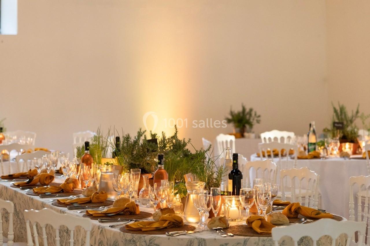 Tables élégamment dressées avec nappes blanches, serviettes jaunes, bougies et décorations végétales dans une salle…