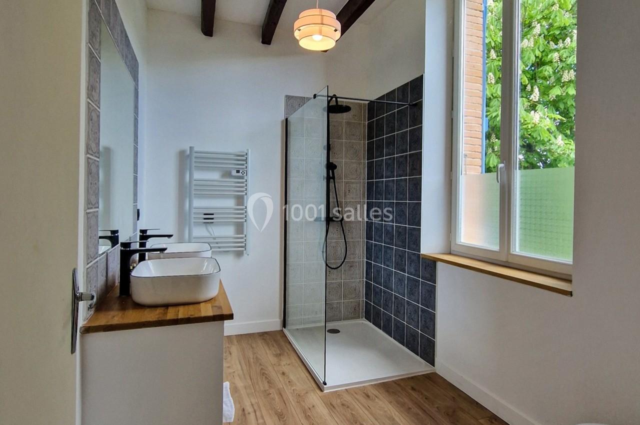 Salle de bain moderne avec douche à l'italienne, double vasque, murs carrelés et fenêtre donnant sur un arbre.