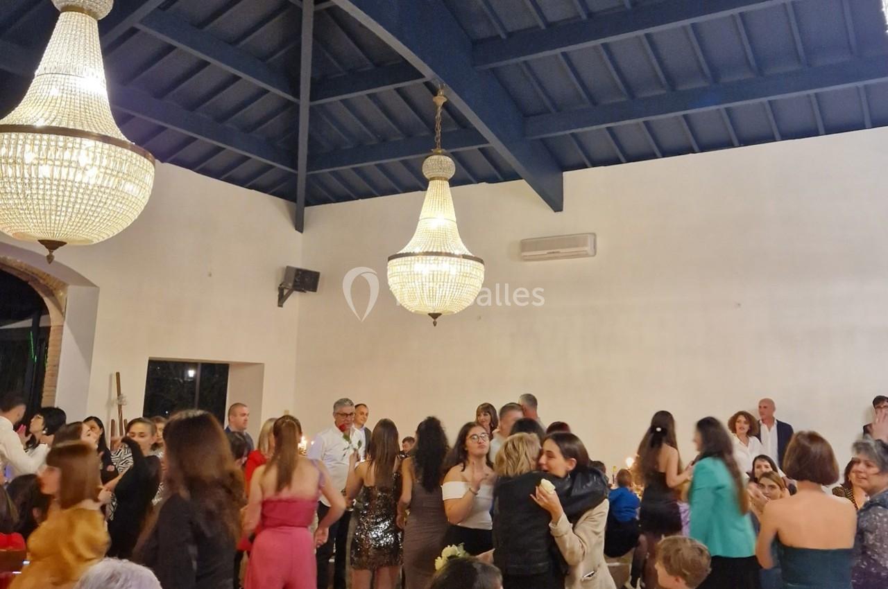 Personnes dansant et discutant lors d'une réception dans une salle éclairée par de grands lustres.