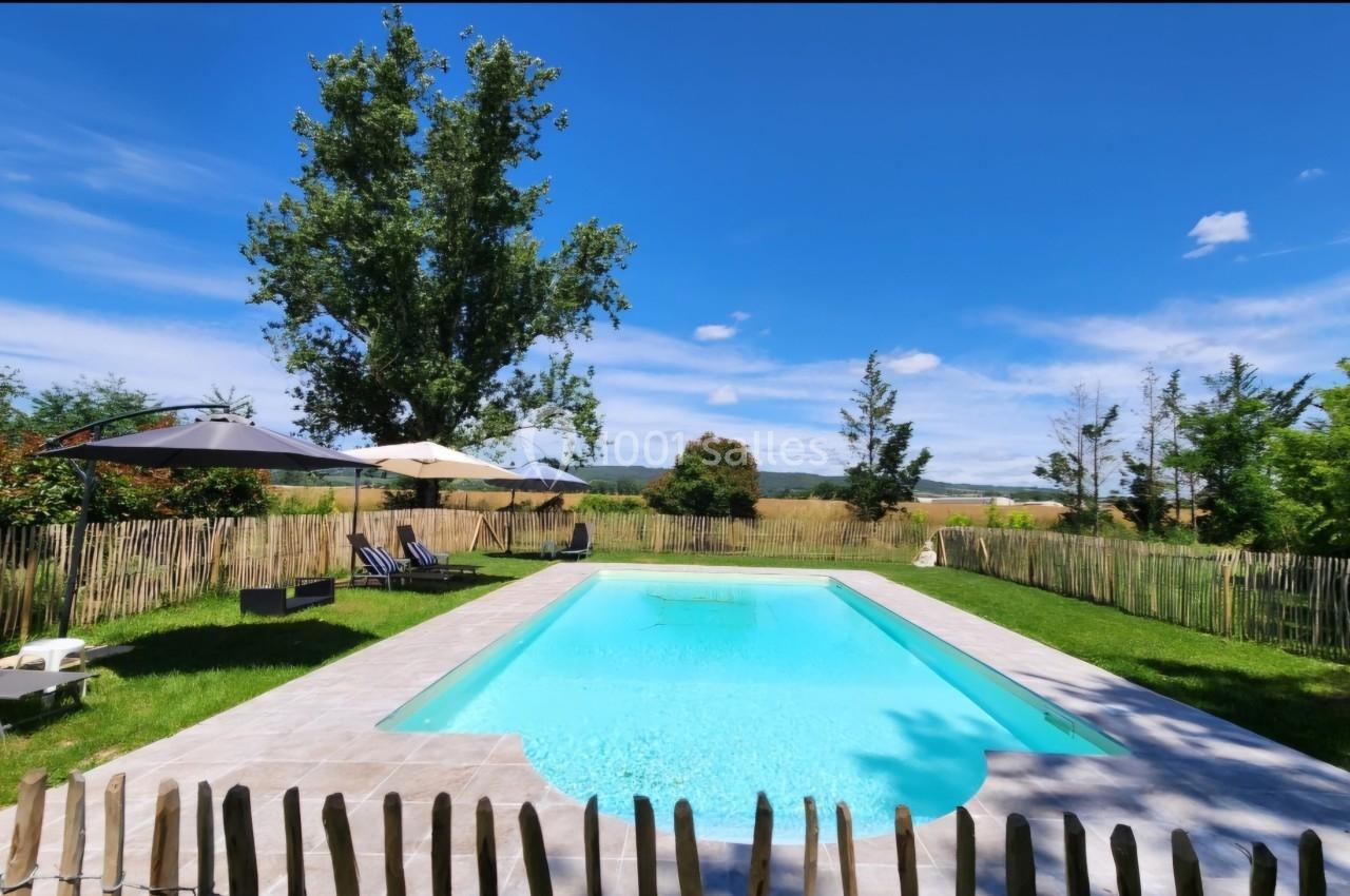 Piscine extérieure entourée de verdure, avec chaises longues et parasols sous un ciel bleu dégagé.