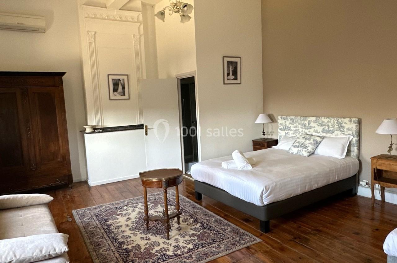 Chambre lumineuse avec lit double, armoire en bois, canapé, tapis et tables de chevet dans un décor classique.