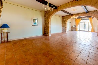 Salle spacieuse avec carrelage au sol, grandes baies vitrées, poutres apparentes et lustres suspendus.