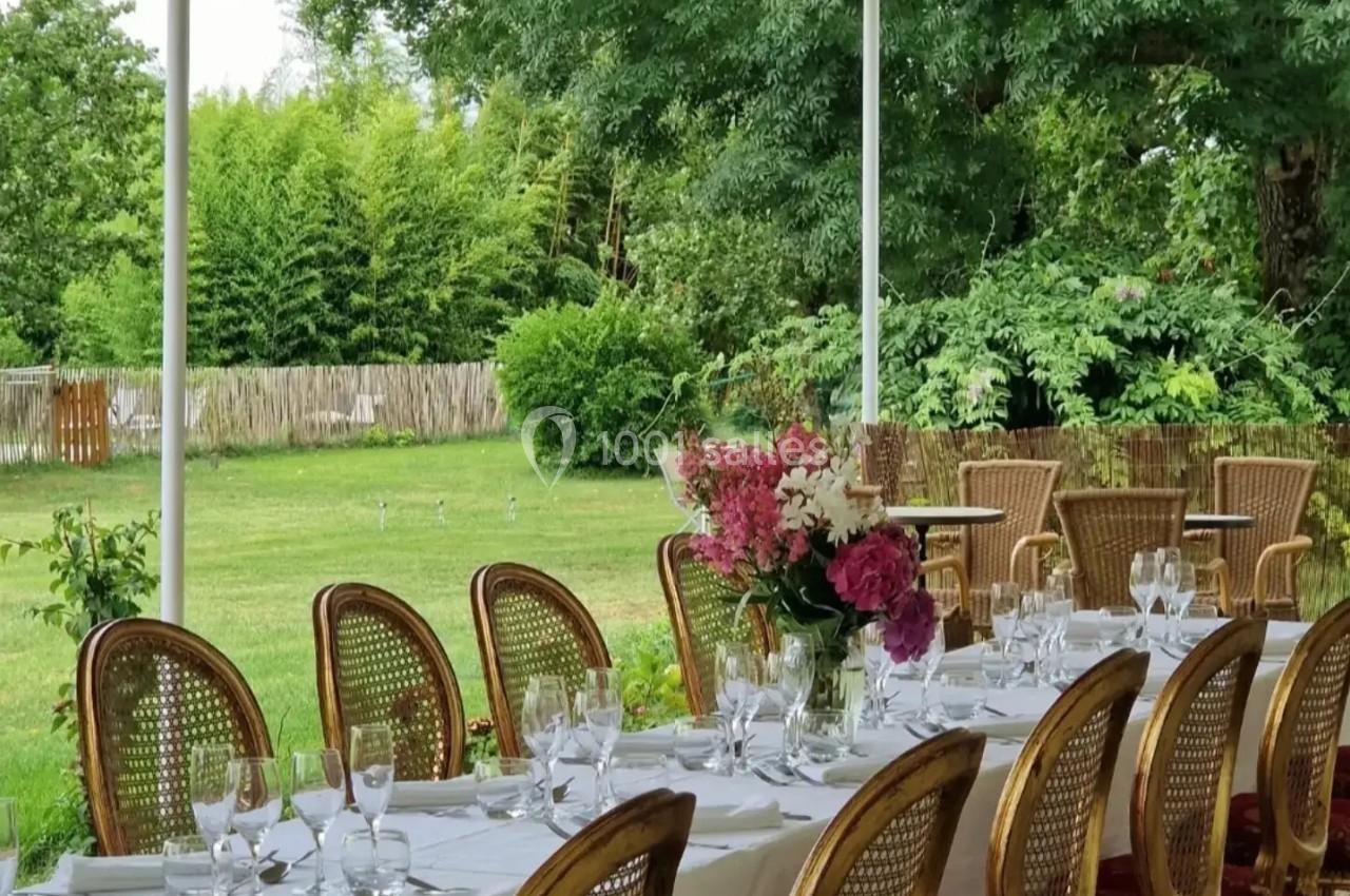 Table dressée avec vaisselle élégante sous une pergola, entourée de chaises en rotin et donnant sur un jardin verdoyant.