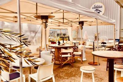 Des personnes assises à des tables sous une pergola ombragée, discutant et partageant un moment convivial.