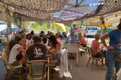 Des personnes assises à des tables sous une pergola ombragée, discutant et partageant un moment convivial.