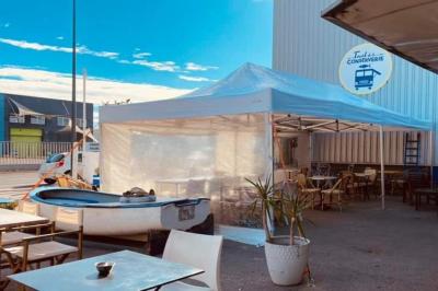 Des personnes assises à des tables sous une pergola ombragée, discutant et partageant un moment convivial.