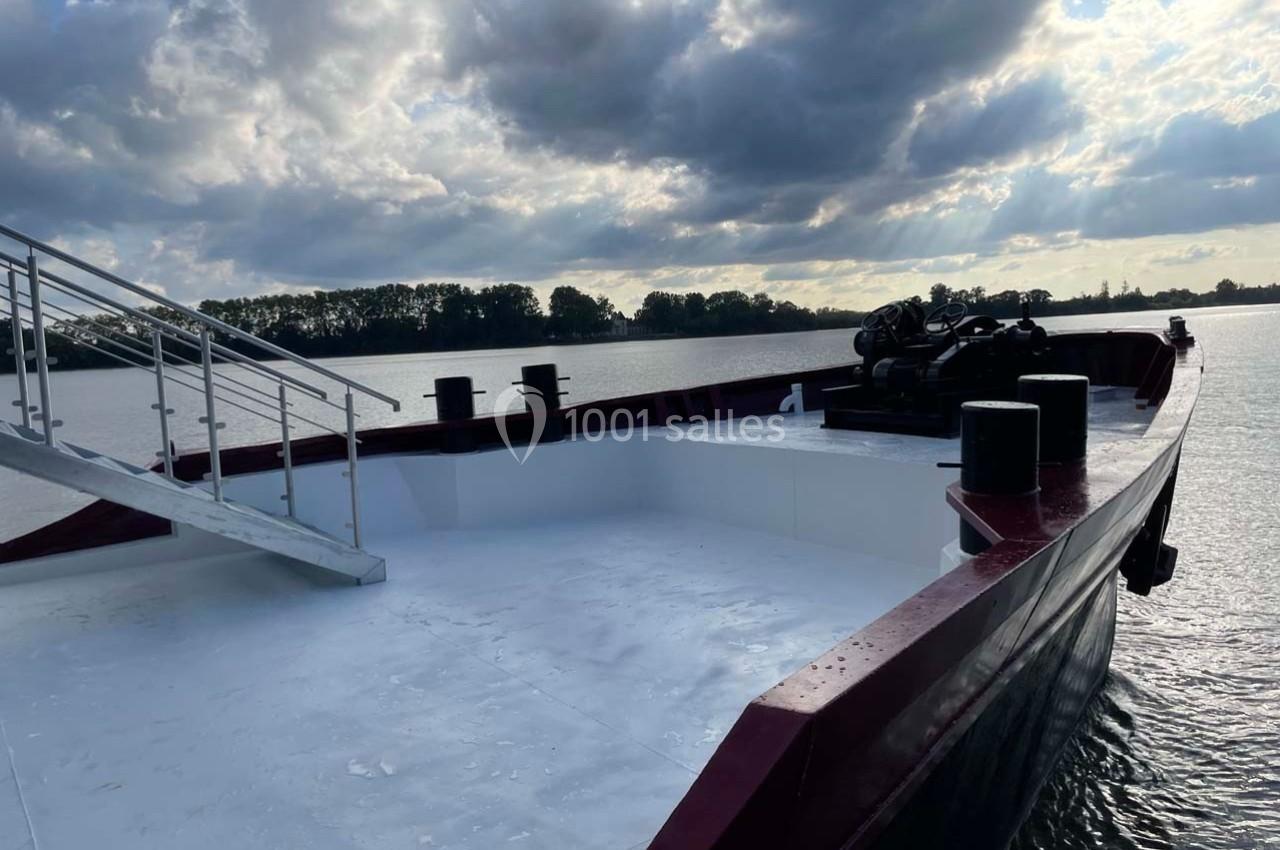 Vue d'un pont de bateau vide sur une rivière, avec un ciel nuageux et des arbres en arrière-plan.