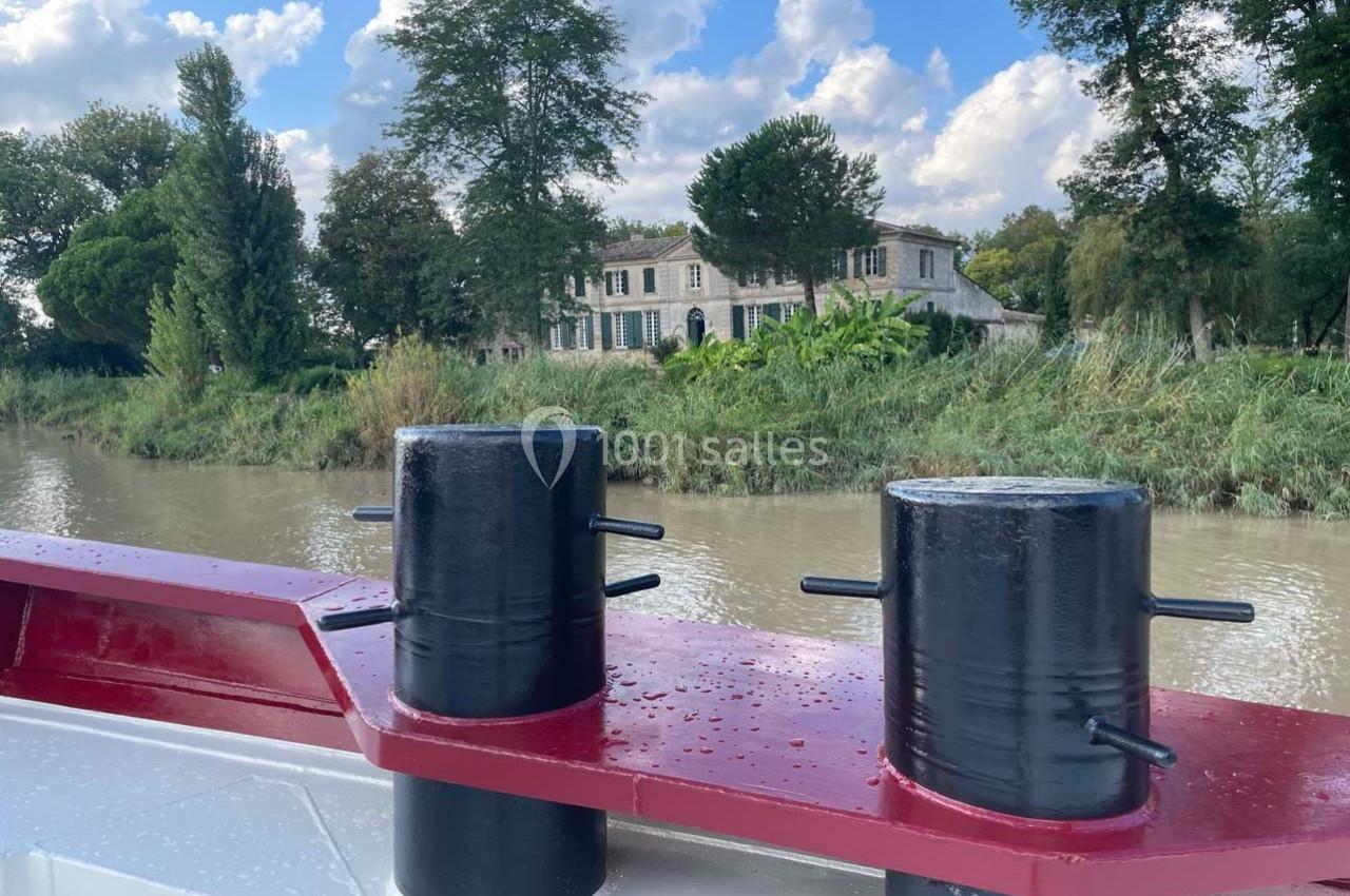 Vue depuis un bateau sur un canal, avec une maison en pierre entourée de végétation en arrière-plan.